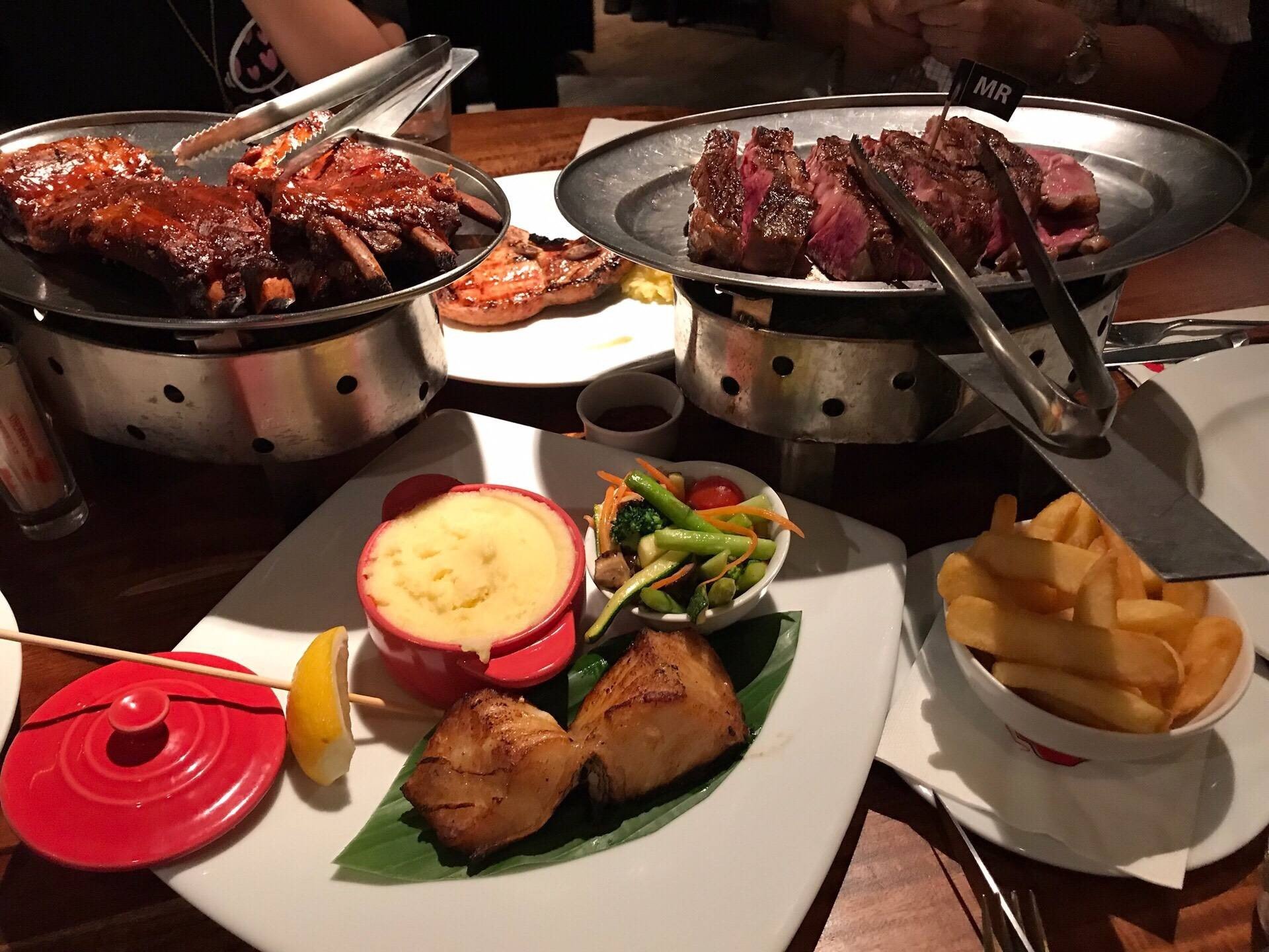 A large meal of ribs, steak, and sides like mashed potatoes and french fries is laid out on a table.