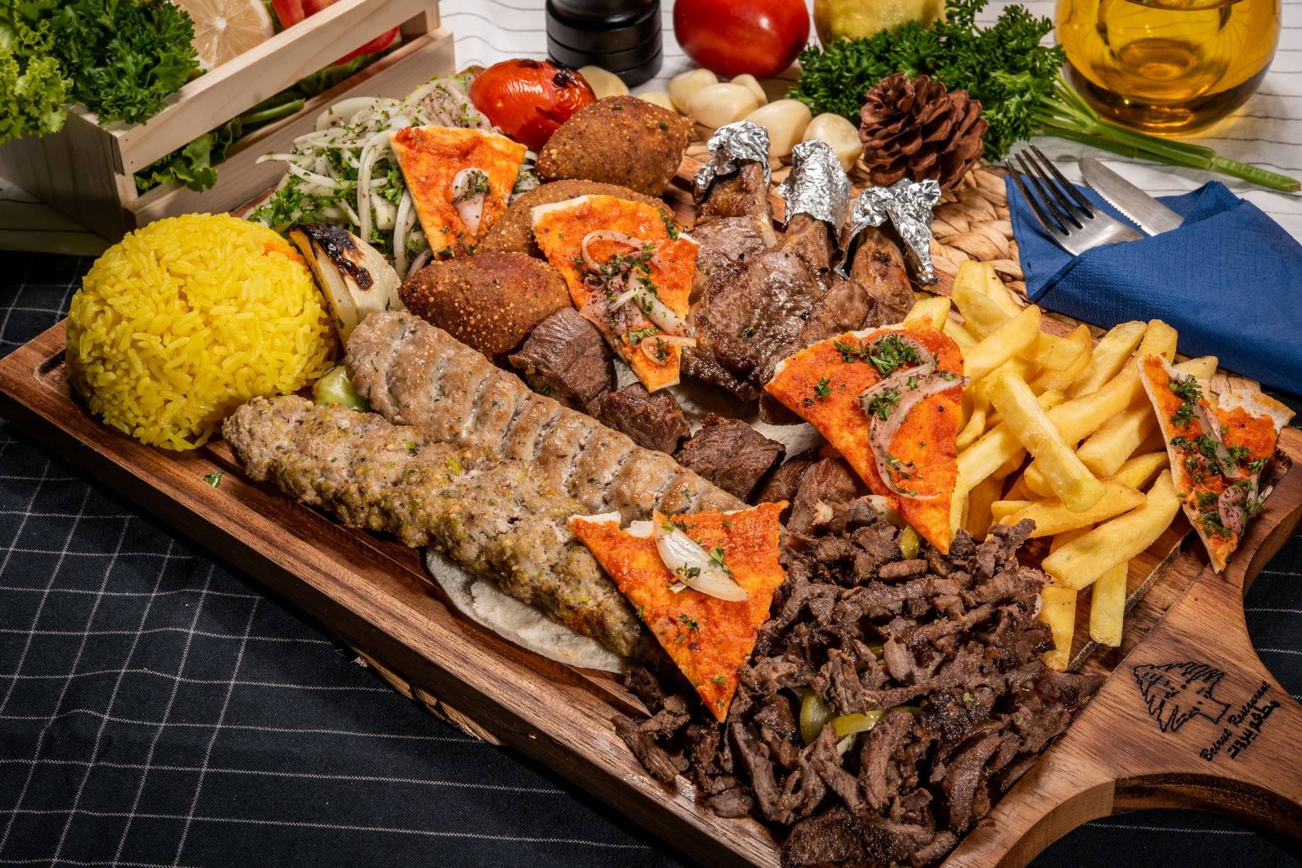 A large platter of various Lebanese dishes, including lamb chops, kebabs, fried kibbeh, rice, and french fries.