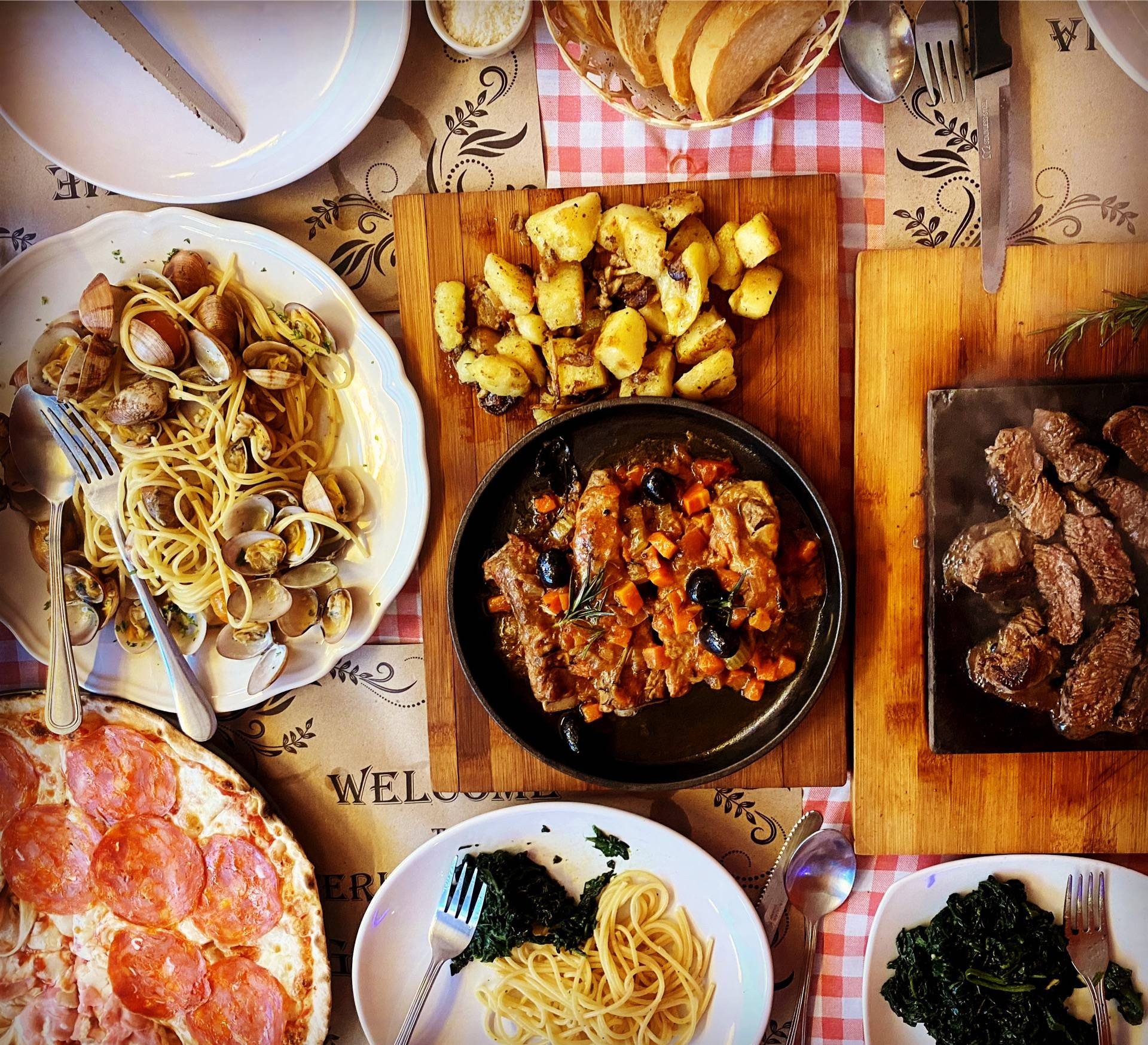 A spread of Italian food featuring spaghetti with clams, pepperoni pizza, braised meat, and steak.